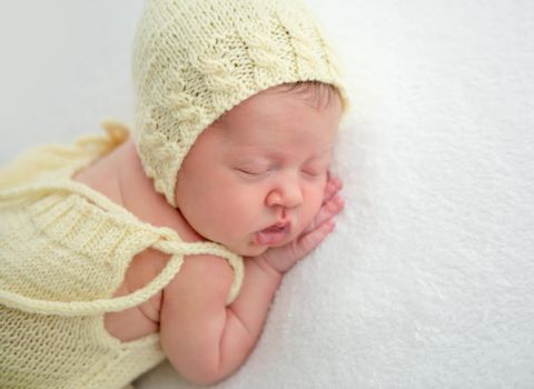 Lovely newborn in yellow suit resting on stomach