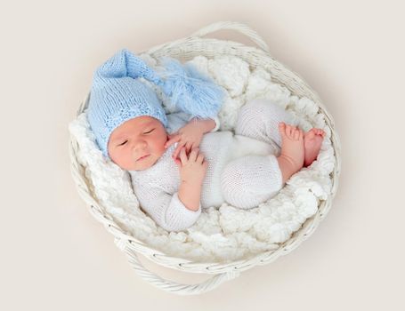 Cute newborn in knitted suit and hat lying in white basket