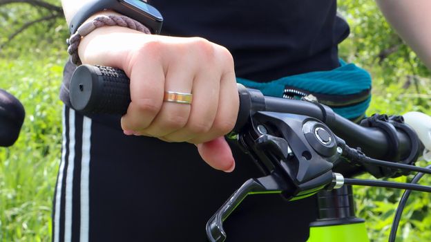 Woman's hand with ring on the handlebars of a mountain bike in the park close-up. The biker leans on the handlebars of the bike