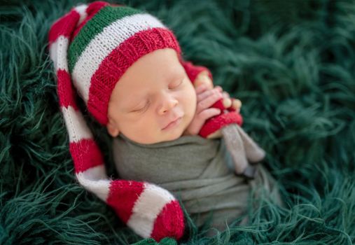 Cute newborn in knitted christmas hat lying on dark green plaid