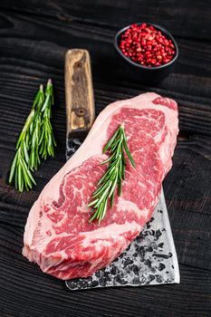 Fresh Raw new york strip beef steak on a butcher meat cleaver. Black wooden background. Top view.