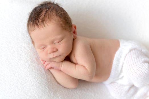 Little baby sweetly sleeping on white knitted pillow and turquoise bedcover