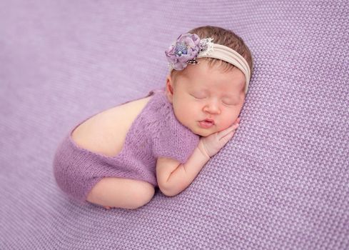 Adorable newborn in knitted purple suit and floral diadem