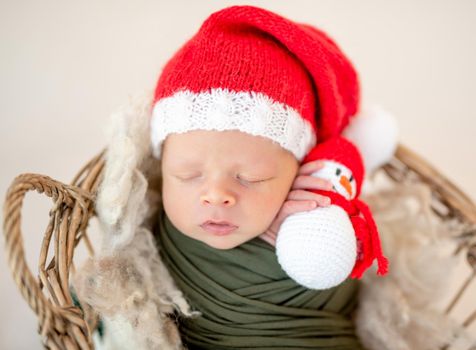 Lovely newborn in santa hat holding snowman toy