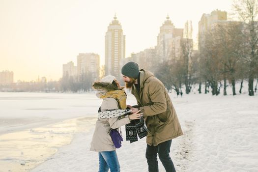 Theme love and date on nature. Young Caucasian heterosexual couple boy and girl kiss hugging warm scarf in winter near a frozen lake in winter. Bearded Man Hugging Woman. Valentine's day holiday.