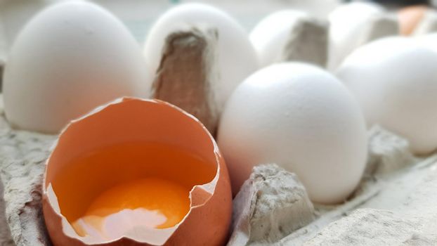 A chicken egg is half broken among other eggs. Close-ups in a paper tray for storage.