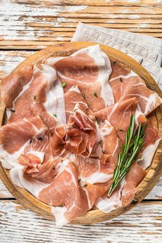 Dry cured parma ham or Prosciutto crudo on a wooden board with rosemary. White wooden background. Top View.