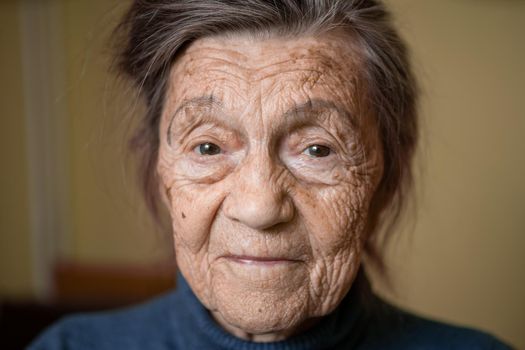 Older cute woman of ninety years old Caucasian with gray hair and wrinkled face looks at camera, cute kind look and smiles.Mature grandmother retired long-liver, theme emotion and mood of old people.