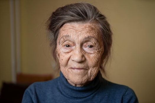 Older cute woman of ninety years old Caucasian with gray hair and wrinkled face looks at camera, cute kind look and smiles.Mature grandmother retired long-liver, theme emotion and mood of old people.