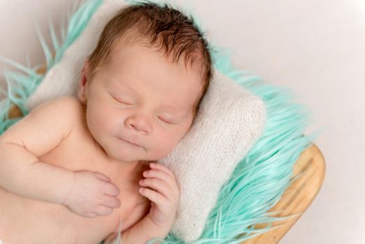 Little baby sweetly sleeping on white knitted pillow and turquoise bedcover