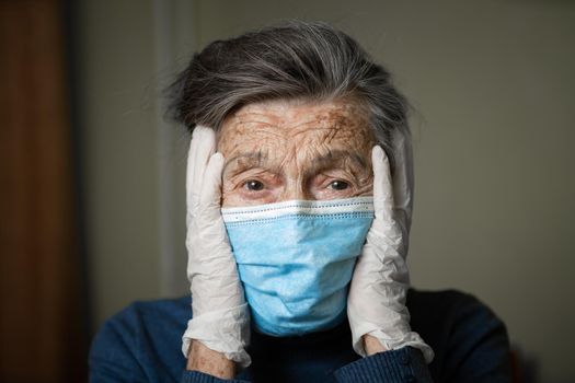 Portrait of an elderly Caucasian woman with wrinkles, wearing a medical mask and gloves, the emotion of fright and unpredictability due to the coronavirus epidemic. Elderly health and medicine theme.