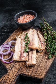 Sardine fish fillet in olive oil on wooden board. Black background. Top view.