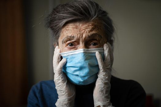 Sad senior woman in protective mask, latex gloves at home during coronavirus pandemic. Stay at home. Old granny retired quarantined epidemic covid 19. Gray hair female in mask infection, bacteria flu.