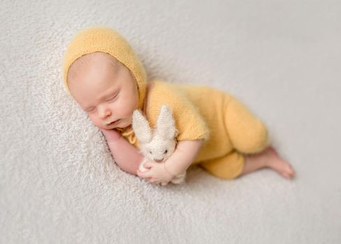 Little baby weared in cute yellow knitted suit sweetly sleeping on the white soft bedcover