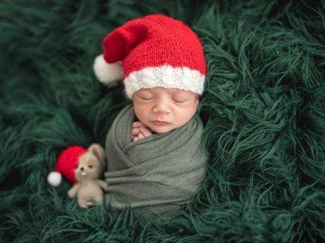 Adorable newborn in santa hat sleeping next to toy