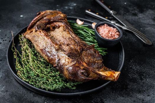 Roasted lamb mutton shoulder meat on a plate with knife and fork. Black background. Top view.