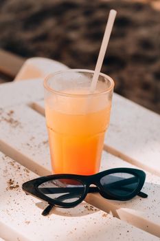 Fresh cold mango smoothie cocktail on tropical beach bright sand. Summer sea vacation and travel concept. Glass of fruit cocktail and sunglasses. Summertime vacation