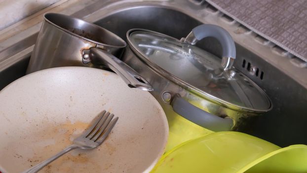 The kitchen utensils in the wash basin need to be washed. A pile of dirty dishes in the kitchen sink. Kitchen utensils need washing. Homework concept