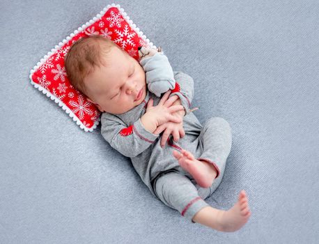 Lovely newborn in sleep suit on tiny decorative pillow