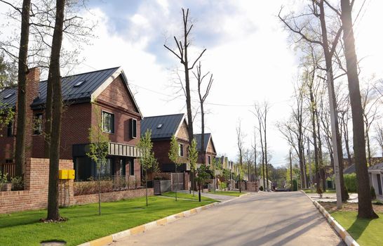 A street with houses and manicured lawns in a typical suburb. Frame made of small brown brick American country houses. Ukraine, Irpin - 07 June 2021