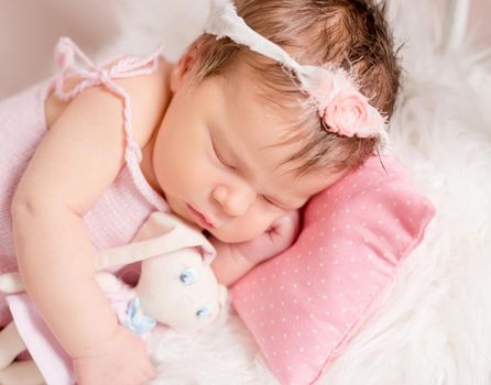 Cute little baby in pink knitted suit sweetly sleeping with toy on the pink dotted pillow