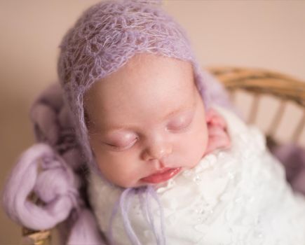 Little cute baby in purple beanie covered with white coverlet sweetly sleeping on purple blanket in the basket