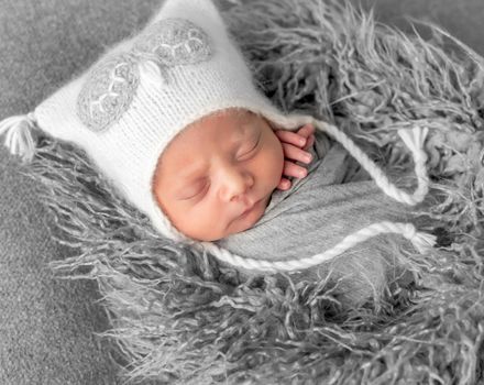 Cute baby in knitted white hat sweetly sleeping on gray pillow with owl toy