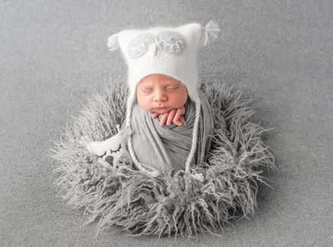 Cute baby in knitted white hat sweetly sleeping on gray pillow with owl toy