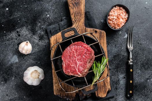 Raw fillet mignon beef steak on a grill with herbs. Black background. Top view.