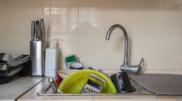 The kitchen utensils in the wash basin need to be washed. A pile of dirty dishes in the kitchen sink. Kitchen utensils need washing. Homework concept