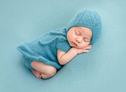 Cute newborn in knitted suit sleeping on blue background