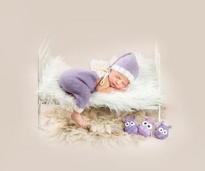 Cute little baby in white and purple knitted suit sweetly sleeping in small bed