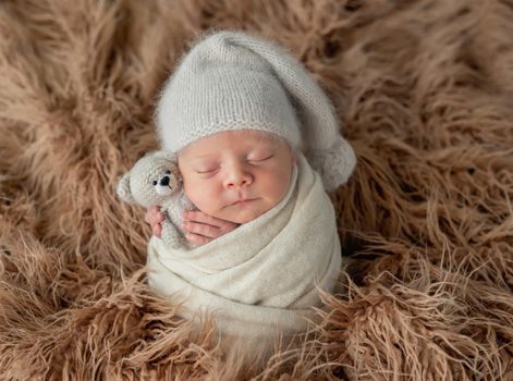 Cute little baby in hat with toy sweetly sleeping covered in blanket
