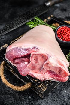 Fresh Raw pork Eisbein knuckle ham in a wooden tray with meat knife. Black Wooden background. Top view.