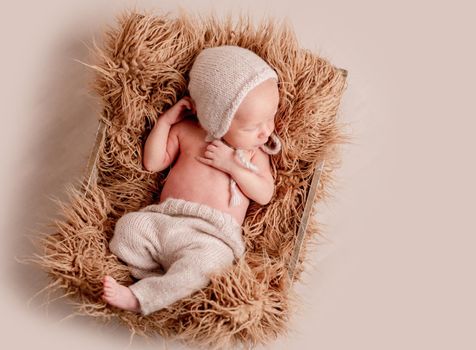 Little cute baby in hat lying covered with light blanket