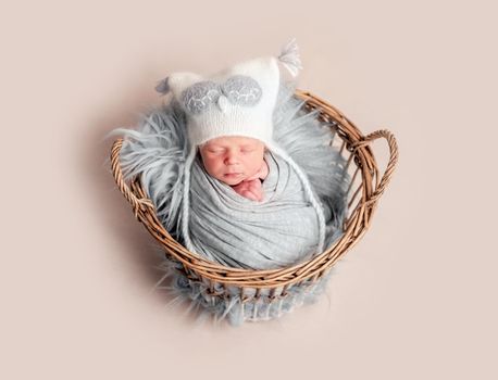 Top view of baby in white knitted hat sleeping in basket covered in blanket