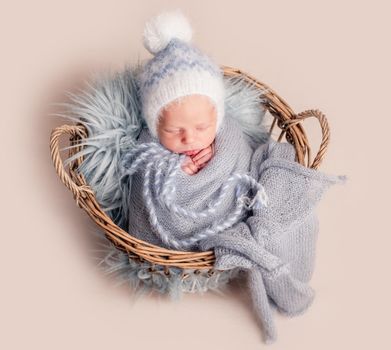Top view of baby in big hat sleeping in basket covered in blue blanket