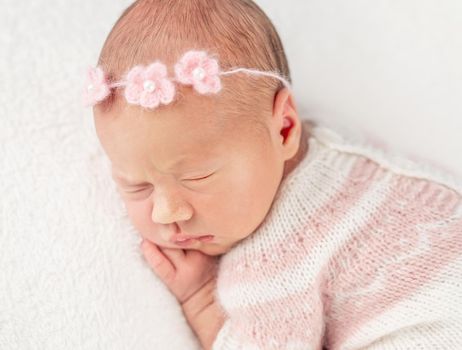 Pretty sleepy little girl in pink and white colored knitted suit and headband, isolated on white background, closeup