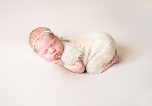 Newborn girl in wool jumpsuit sleeping on light background