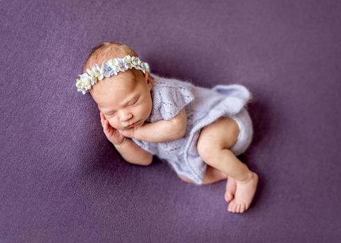 Quiet newborn in cute knitted violet blue wool jacket and floral headband