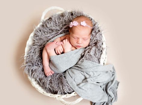 Newborn baby in grey blanket with floral headband sleeping in basket