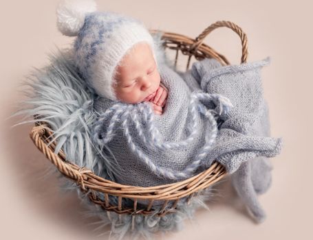 Top view of baby in big hat sleeping in basket covered in blue blanket