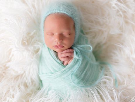 Newborn boy lying wrapped in a blanket with favorite knitted blue teddy bear