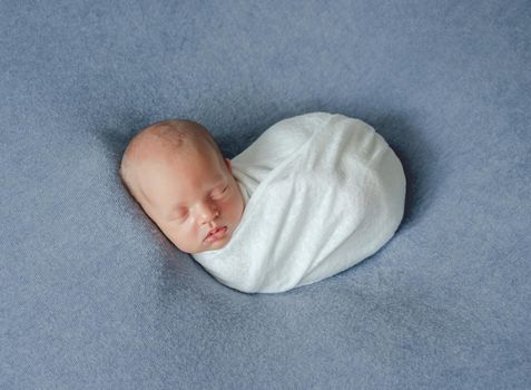 Little newborn wrapped in blue blanket resting in room