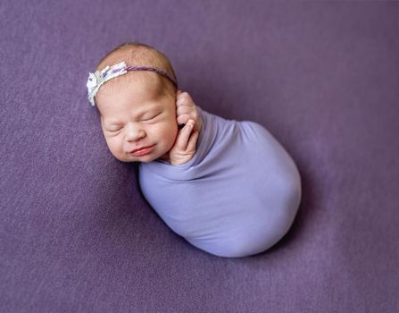 Sleeping newborn girl in the purple violet pink fabric background