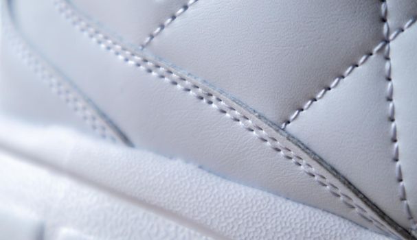 Close-up of synthetic fabric with white diamond stitching and white rubber sole. Sport shoes. Quilted fabric in white or light color, texture