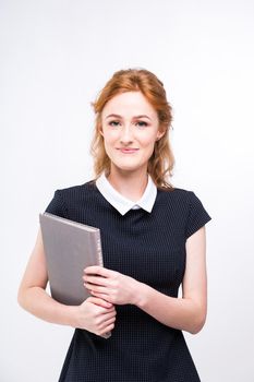 Beautiful girl with red hair and gray book in hands dressed in black dress on white isolated background.