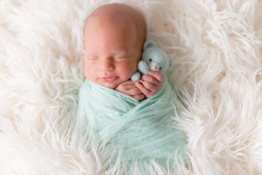 Newborn boy lying wrapped in a blanket with favorite knitted blue teddy bear