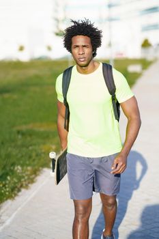 Black man with afro hair, going for a workout in sportswear and a skateboard.