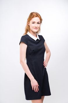 beautiful young girl student, secretary or business lady with charming smile and red curly hair in black dress in white dot and white collar on white gray background in studio.